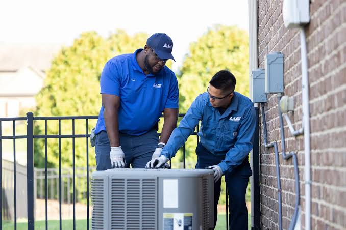 Two HVAC technicians positioning a residential air conditioning unit